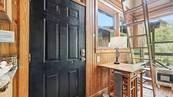 A wooden door, a window with a view, a table with a lamp, and a pet bed.