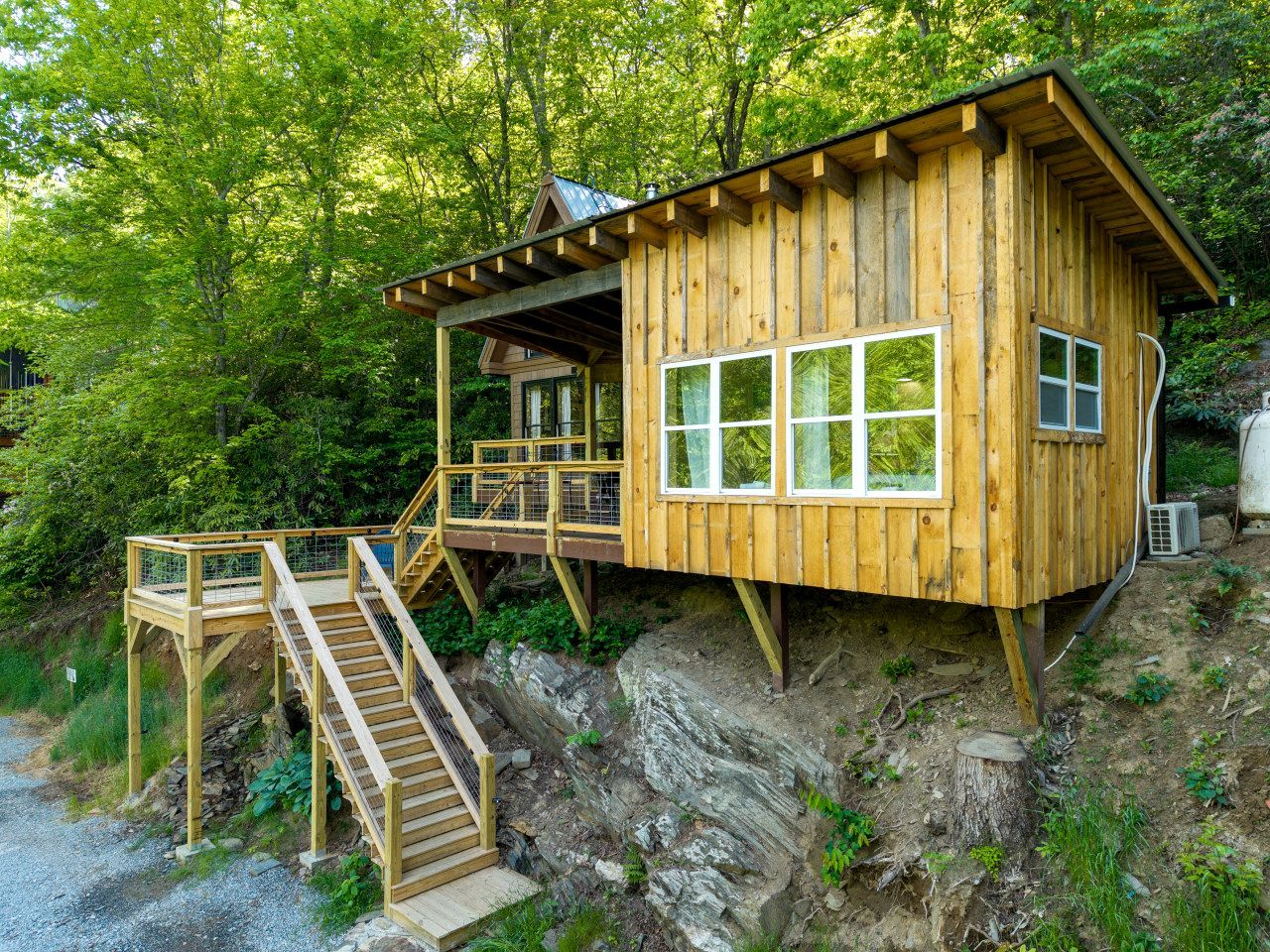 Eine Holz-Blockhütte mit Balkon, Treppe und Blick auf den umliegenden Wald.