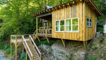Eine Holz-Blockhütte mit Balkon, Treppe und Blick auf den umliegenden Wald.