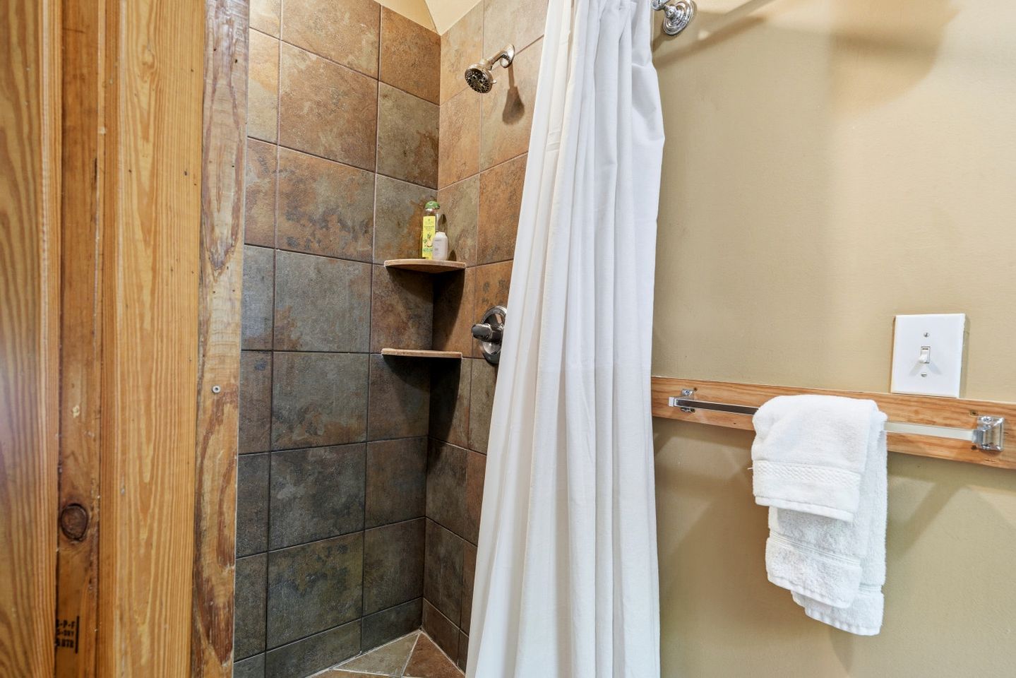Eine Dusche mit Vorhang, ein Holzregal mit Toilettenartikeln und ein Handtuchhalter mit Handtüchern.