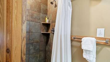 Eine Dusche mit Vorhang, ein Holzregal mit Toilettenartikeln und ein Handtuchhalter mit Handtüchern.