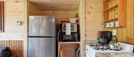 A compact kitchen with a refrigerator, microwave, stove, and wooden cabinets.
