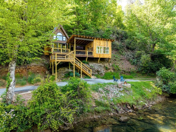 A wooden cabin with a deck, a staircase, and a view of a river.