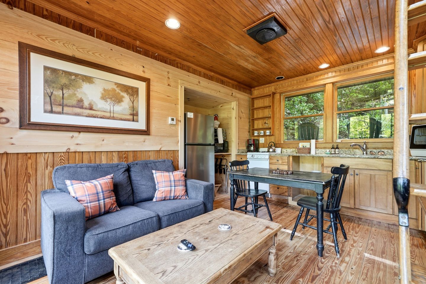 A cozy cabin interior with a sofa, coffee table, dining table, chairs, kitchen area, and a framed picture on the wall.