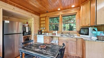 A wooden cabin kitchen with a refrigerator, stove, microwave, and a table with chairs.