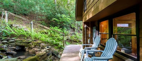 Une terrasse en bois avec des fauteuils Adirondack, un mur de pierres et un petit ruisseau.