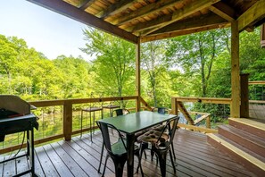 A covered outdoor deck with a table and chairs, overlooking a forested area.