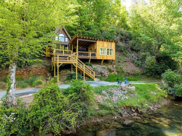 A wooden cabin with a deck, a staircase, and a view of a river.