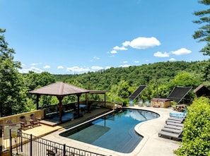A swimming pool with a wooden deck, lounge chairs, and a gazebo.