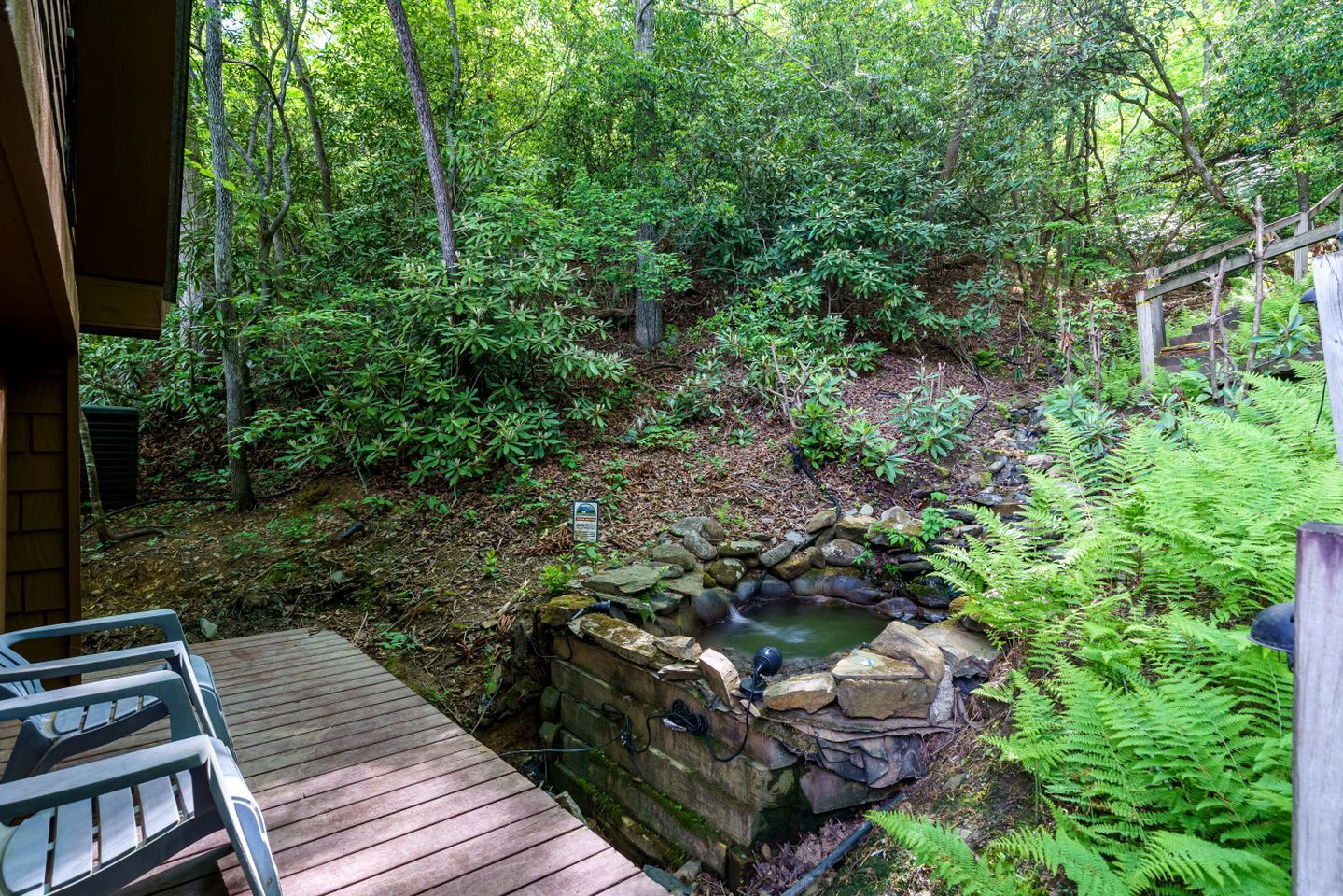 A wooden deck leading to a stone hot tub surrounded by dense forest.