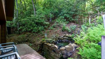 A wooden deck leading to a stone hot tub surrounded by dense forest.