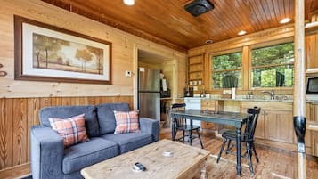 A cozy cabin interior with a sofa, coffee table, dining table, chairs, kitchen area, and a framed picture on the wall.