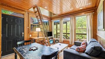 Ein Holzinterieur mit einem Esstisch, Stühlen, einer Couch, einem Fernseher und einer Leiter.