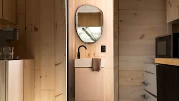 A wooden interior with a sink, mirror, and microwave.