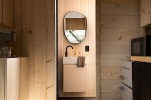A wooden interior with a sink, mirror, and microwave.