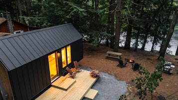 A cabin with a deck, a fire pit, and a view of a forested area.