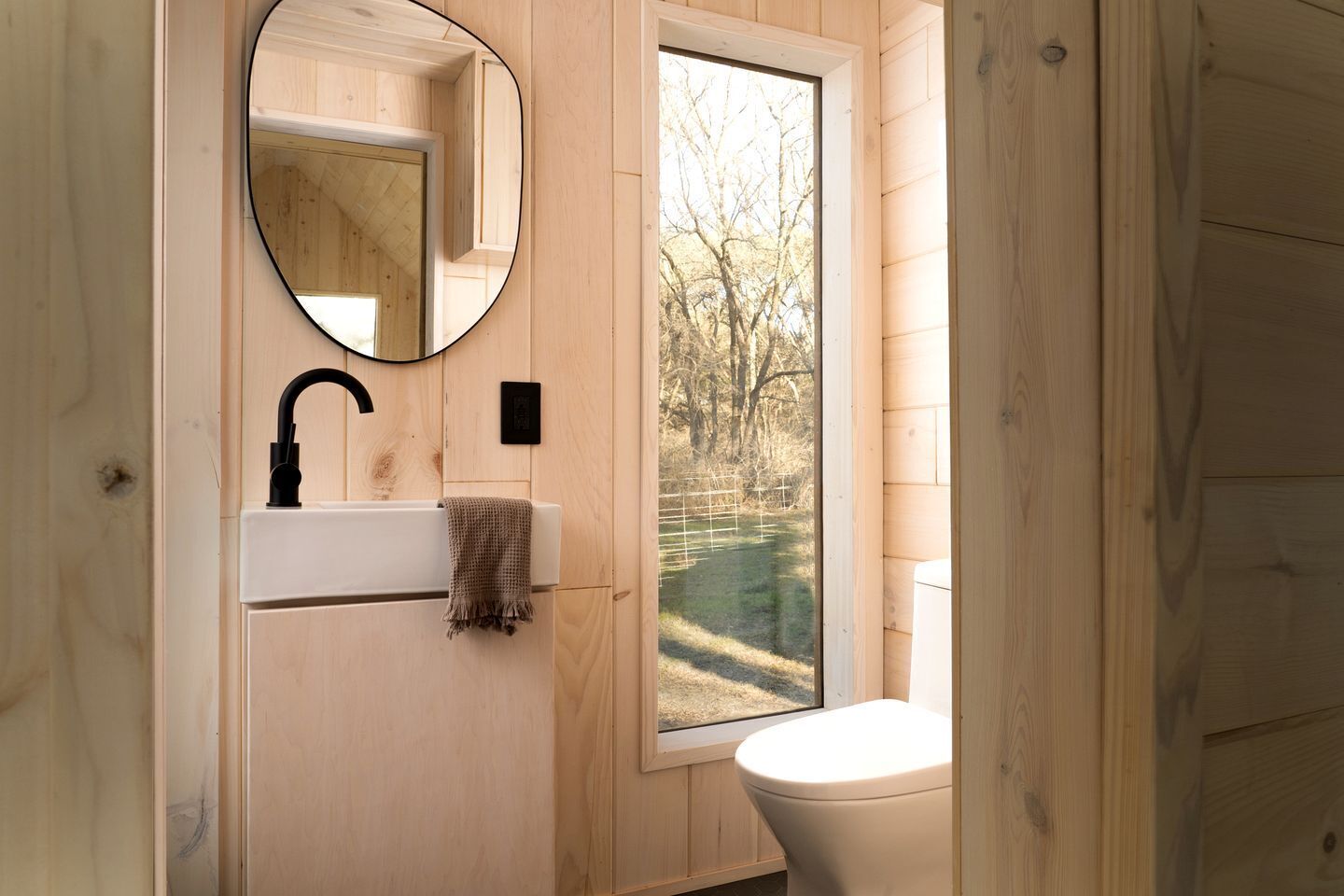 A wooden bathroom with a sink, mirror, and toilet.
