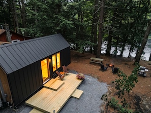 A cabin with a deck, a fire pit, and a view of a forested area.