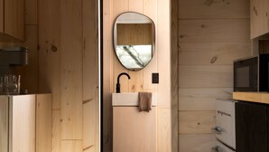 A wooden interior with a sink, mirror, and microwave.