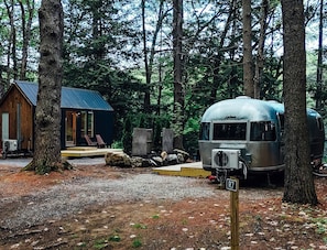 A forested campsite with a cabin and a vintage camper.