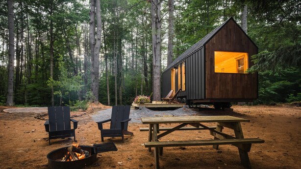 A cabin with a fire pit, two chairs, and a picnic table in a forest setting.