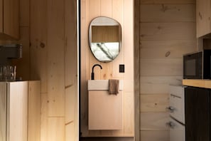 A wooden interior with a sink, mirror, and microwave.