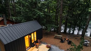 A cabin with a deck, a fire pit, and a view of a forested area.