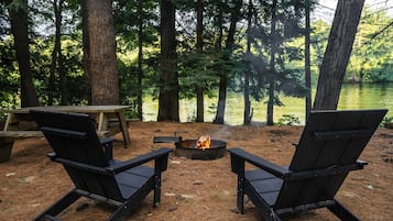 Um camping com duas cadeiras Adirondack, um braseiro e uma mesa de piquenique.