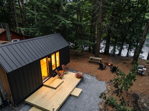 Une cabane dotée d’une terrasse, d’un foyer extérieur et offrant une vue sur une zone boisée.