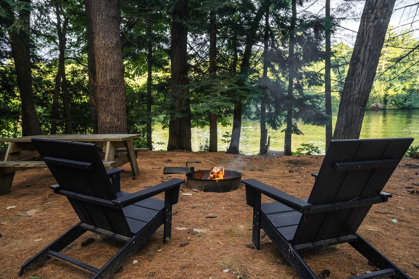 A campsite with two Adirondack chairs, a fire pit, and a picnic table.