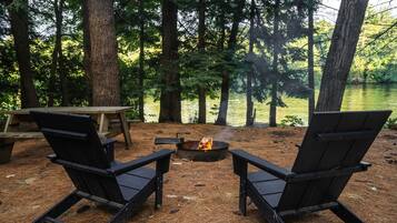 A campsite with two Adirondack chairs, a fire pit, and a picnic table.