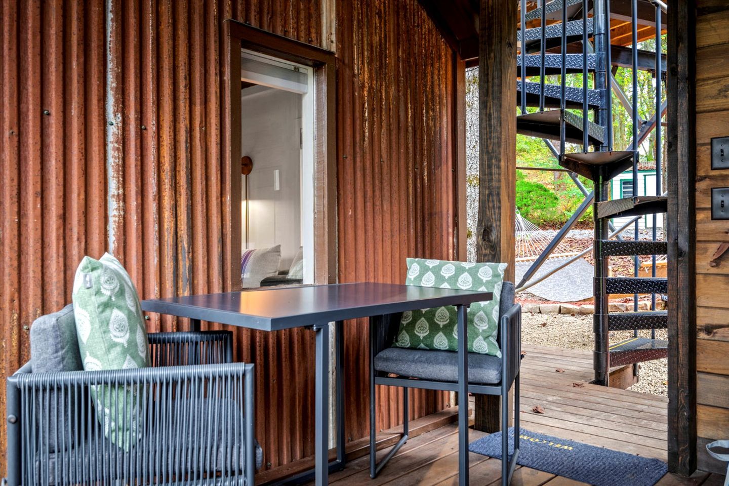 A wooden cabin with a balcony, a table with chairs, and a spiral staircase.