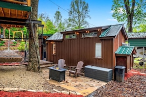 A wooden cabin with a patio, two Adirondack chairs, a fire pit, and a trash can. - Beautiful Cabin with Fire Pit in Hayesville, North Carolina (Hayesville)