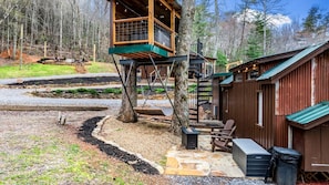 A cabin with a wooden deck, a treehouse, and a stone patio. - Beautiful Cabin with Fire Pit in Hayesville, North Carolina (Hayesville)