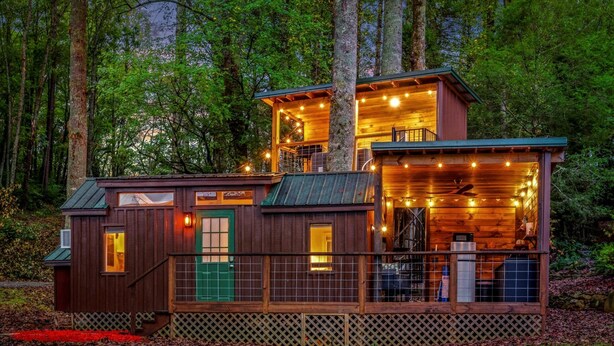 A cabin with a green door, a balcony, and a covered outdoor area with string lights.