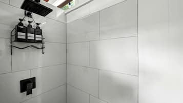 A shower area with white tiles, a black showerhead, and a shelf with toiletries.