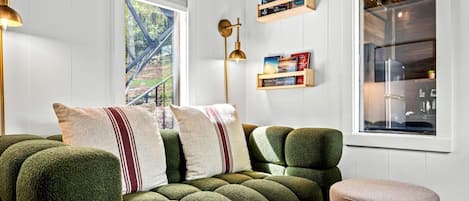 Una stanza accogliente con un divano imbottito verde, un poggiapiedi rotondo e una libreria piena di libri.