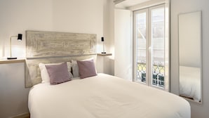 A bedroom with a large bed, a rustic headboard, two bedside lamps, and a balcony with a metal railing. - Downtown Modern Apartments by Homing (Lisbon)