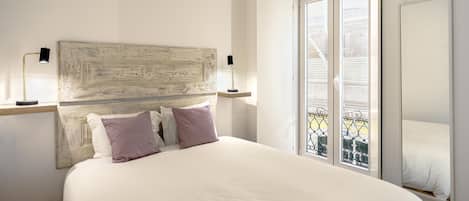Une chambre à coucher avec un grand lit, une tête de lit rustique, deux lampes de chevet et un balcon doté d’une rambarde en métal.