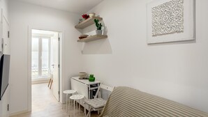 A small, bright room with a bed, a desk, and two chairs. There are shelves with decorative items and a wall art piece. - Downtown Modern Apartments by Homing (Lisbon)
