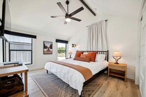 A bedroom with a bed, a ceiling fan, a nightstand with a lamp, a window with curtains, and a rug.