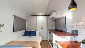 A compact bedroom with a bed, bedside table, and a small kitchenette.