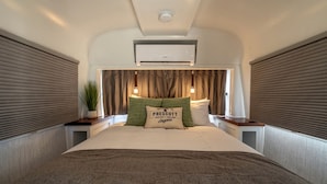 Ein Schlafzimmer mit Bett, Nachttisch, Topfpflanze, Kissen mit Aufdruck und Klimaanlage.