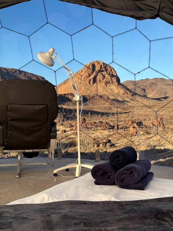 Una tienda de campaña con estructura hexagonal, una silla, una lámpara y toallas sobre un tapete.