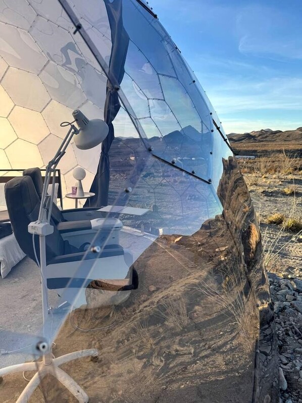 A transparent dome structure with a chair and desk inside, set against a mountainous backdrop.