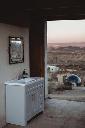 A bathroom with a white sink, a mirror, and a view of a desert landscape through an open door.