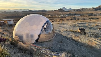 Une structure en forme de dôme géodésique, située dans un paysage désertique, avec des montagnes en arrière-plan.