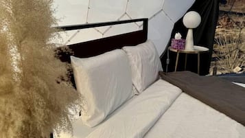 Un lit avec une literie blanche, une tête de lit noire et un panier en osier contenant des plumes d’herbe des pampas.