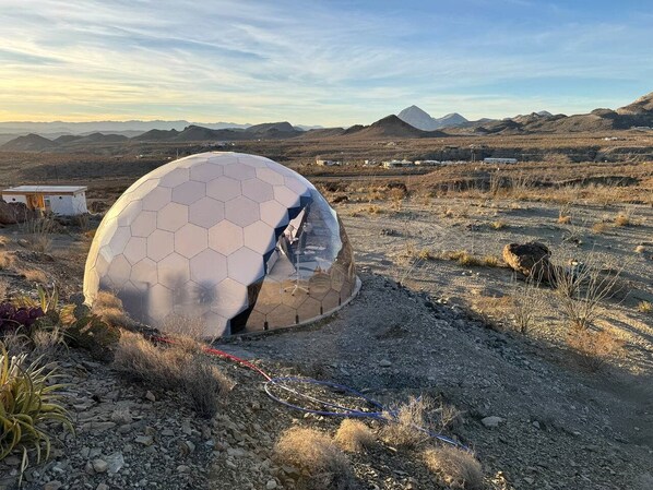 Una estructura de domo geodésico en un paisaje desértico con montañas al fondo.