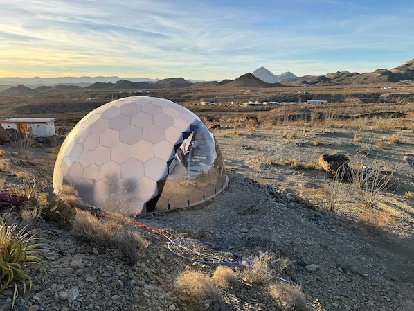 Une structure en forme de dôme géodésique, située dans un paysage désertique, avec des montagnes en arrière-plan.